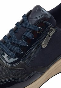 Sneaker blu navy caratterizzato da una combinazione di pelle verniciata lucida e tessuto testurizzato, con chiusura a lacci e dettaglio con zip laterale.