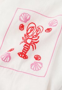 Homard rouge brodé entouré de coquillages rouges et roses sur un tissu blanc, encadré d'une bordure brodée rose.