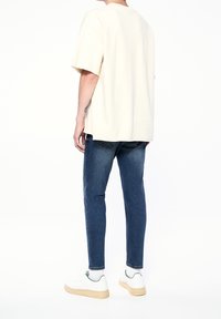 Camiseta beige de gran tamaño con mangas cortas combinada con jeans ajustados azul y zapatillas blancas, con acentos verdes en el calzado.