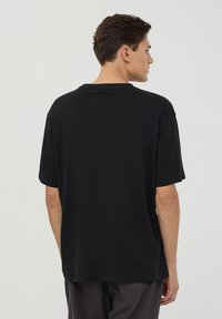 Maglietta nera in cotone con vestibilità rilassata, maniche corte e scollo rotondo, mostrata da dietro con una texture liscia.