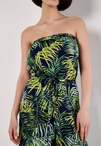 Mono sin tirantes en azul marino con estampado de hojas de palma verdes, cuerpo fruncido, cintura elástica y cordón ajustable. Textura de tela suave.