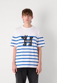 Gestreiftes T-Shirt in Weiß und Blau mit einem schwarzen Grafiklogo "HUGO" auf der Vorderseite. Kurze Ärmel, lockere Passform, Baumwollmaterial, lässiges Design.