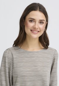 Blouse à carreaux marron et crème avec un col rond et des manches longues, présentant un tissu doux et texturé ainsi que des détails plissés subtils aux épaules.