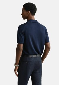 Námořnické polo tričko s krátkým rukávem a přiléhavým střihem, s klasickým límečkem a hladkou texturou, v kombinaci s dobře střiženými tmavými kalhotami.