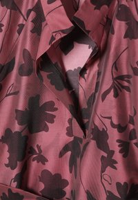 Hosszú ujjú blúz rózsaszín anyagból, fekete virágmintákkal, texturált szövettel és kivágott gallér dizájnnal.