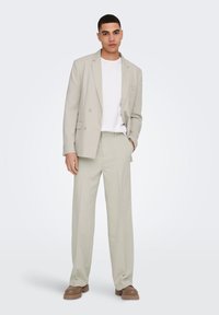 Traje gris claro con blazer de doble botón y pantalones a medida. Combinado con una camiseta blanca y calzado marrón claro. Textura suave.