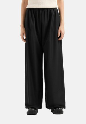 Pantaloni neri a gamba larga con vita elastica, texture liscia e vestibilità rilassata. Abbinati a calzature nere spesse.