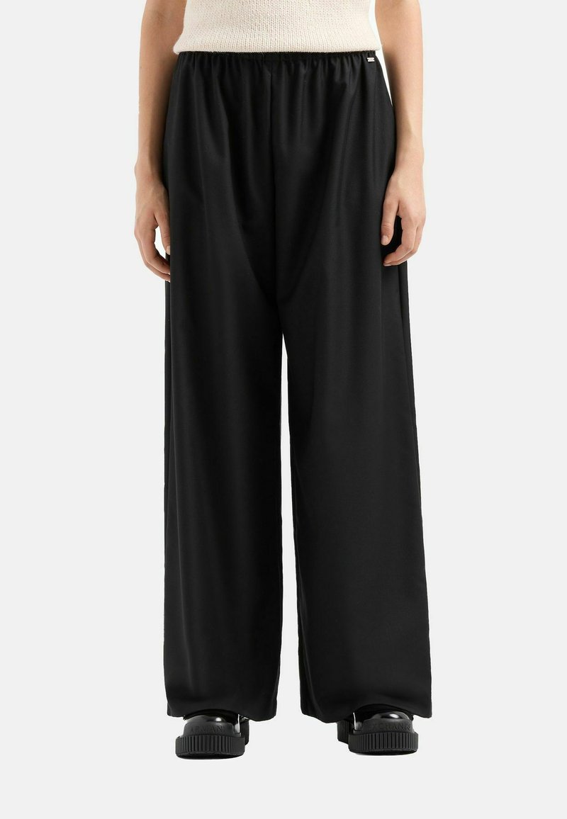 Pantaloni neri a gamba larga con vita elastica, texture liscia e vestibilità rilassata. Abbinati a calzature nere spesse.