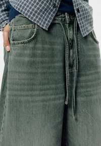 Groene denim broek met een relaxte pasvorm, voorzien van een taille met trekkoord en zijzakken, afgewerkt met subtiele vervaging en stikdetails.