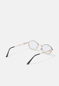 Ochelari rotunzi din metal aurit cu lentile clare. Prezintă o balama decorativă și brațe negre cu un finisaj lucios.