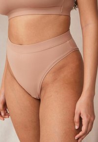 Sous-vêtements taille haute en tissu beige doux avec une texture lisse, dotés d'une large bande élastique à la taille et de détails de couture minimaux.