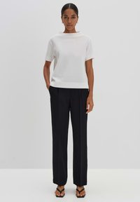 White short-sleeve top with a textured pattern, paired with tailored black trousers and flat black sandals, creating a sleek silhouette.