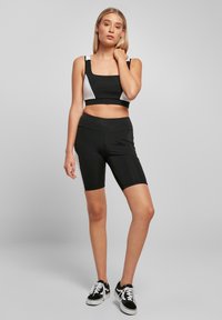 Musta urheiluvaatesetti, joka sisältää lyhyen topin suorakulmaisella pääntiellä ja valkoisilla sivupaneeleilla, yhdistettynä korkeavyötäröisiin mustiin pyöräilyshortseihin.