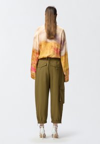 Majica dugih rukava od višebojnog gradijentnog materijala, uparenih s maslinasto zelenim uskim cargo hlačama koje imaju bočne džepove i elastične manžete.