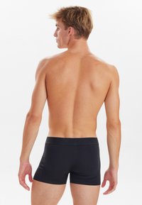 Pantalones cortos de boxeo negros hechos de tela suave, con un ajuste ceñido y una cintura elástica. El diseño es sencillo, sin patrones ni logotipos.