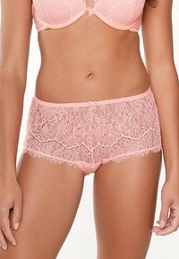 Lace panties in soft pink with floral patterns, featuring a mid-rise cut, scalloped edges, and a small bow accent at the waistband.
