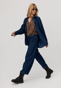 Jeansowa koszula i spodnie w ciemnoniebieskim kolorze, zestawione z leopardzim wzorem. Całość dopełniają czarne buty na sznurówki i okrągłe okulary przeciwsłoneczne.