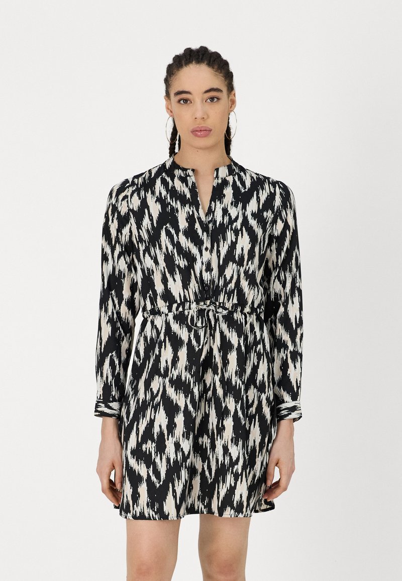 Langärmliges Kleid im schwarz-weißen Ikat-Muster, mit einer taillierten Taille und einem silbernen Ringdetail sowie einem knopfnden Ausschnitt.