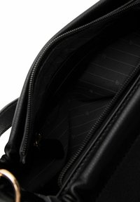 Interno di una borsa a tracolla in pelle nera, caratterizzato da una superficie liscia, un delicato motivo a righe e una chiusura con cerniera dotata di accessori color oro.