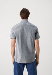 Kortärmad, ljusgrå skjorta med krage, subtil textur, rak skärning och rundad fåll, bärs med blå jeans.