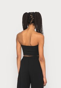 Top corto negro sin tirantes con textura suave, combinado con pantalones negros de pierna ancha y cintura alta. La vista trasera resalta el diseño elegante del top.