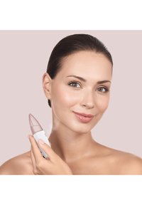 Dispositif de nettoyage facial avec un embout effilé de couleur rose translucide et un corps blanc. Texture lisse ; tenu par une personne à la peau claire.