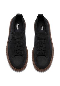 Chaussures en daim noir avec une semelle en caoutchouc, présentant des lacets, une finition texturée et un design de semelle extérieure nervurée distinctif. Logo imprimé à l'intérieur.