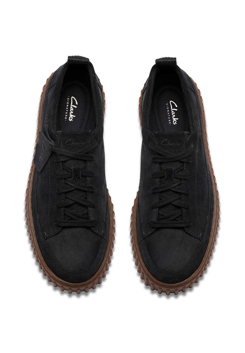 Schwarze Wildlederschuhe mit Gummisohle, ausgestattet mit Schnürsenkeln, einer strukturierten Oberfläche und einem markanten gerippten Außensohlen-Design. Logo auf der Innenseite gedruckt.