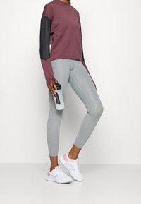 Maroonowa bluza z czarnymi rękawami, szare legginsy i białe-różowe sneakersy. Osoba trzyma butelkę wody. Gładkie tekstury, sportowy krój.