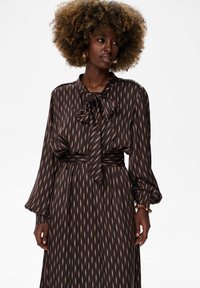 Czarna sukienka z długim rękawem i kokardą przy dekolcie, zdobiona pionowymi pasami w kolorze złotym i brązowym. Miękka, zwiewna tkanina z wcięciem w talii.