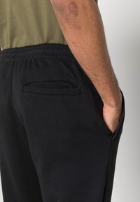 Pantaloni da jogging neri con un elastico in vita e una tasca laterale, realizzati in un morbido misto cotone. Presentano una superficie liscia e un design semplice.