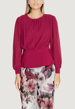 Blusa bordeaux con maniche lunghe a sbuffo, scollatura arricciata e vita a peplo. Abbinata a pantaloni floreali a fantasia in tonalità di rosa e grigio.