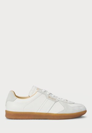 Bele usnjene snežke z sivo semiš okrasitvijo. Imajo rjavo gumijasto podplat in zlate logotipne detajle na strani in jeziku. Zavezovanje.