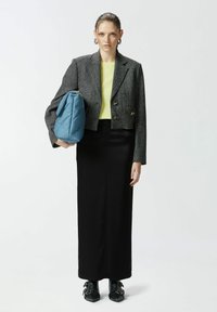 Srebrno siva jakna od tvida, žuti gornji deo, crna duga suknja, plava dugmad torbica i crne cipele sa špicastim krajevima i metalnim detaljima. Jednostavan dizajn.