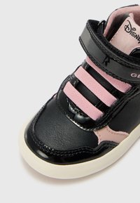 Tenis de verniz preto com tiras de tecido rosa, detalhes em bege, bico arredondado e sola de borracha branca. Marca da Disney visível no interior.