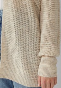 Beige gestrickte Strickjacke mit strukturiertem Muster, weiten Ärmeln und gerippten Bündchen, gefertigt aus einem weichen und gemütlichen Stoffmix.
