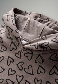 Sudadera marrón con un patrón de corazones repetido en negro, con un cuello doblado y una textura de tela suave.