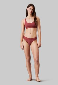 Set di reggiseno e bikini Calvin Klein in un colore ruggine tenue. Tessuto testurizzato con un elastico largo che presenta dettagli del logo. Design semplice e aderente.