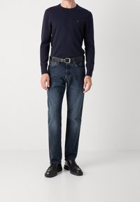 Chemise marine à manches longues, jean bleu foncé, ceinture en cuir noire et chaussures habillées noires. Coupe décontractée avec une texture lisse et un minimum de détails.