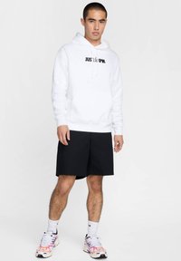 Sudadera blanca con texto negro "JUST DO IT", combinada con pantalones cortos negros y zapatillas deportivas multicolores. Textura suave, corte relajado.