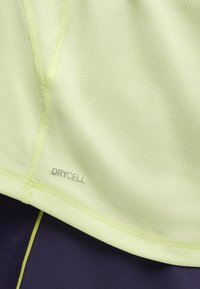 T-shirt de sport jaune clair texturé avec logo réfléchissant "DRYCELL" sur une couture, associé à un matériau bleu marine foncé en dessous. Design respirant.