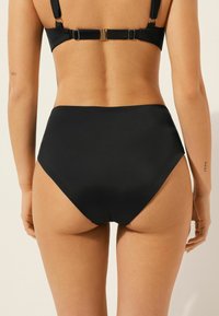 Bas de bikini noir taille haute en tissu lisse, avec un design sans couture, une silhouette minimaliste et sans motifs visibles.