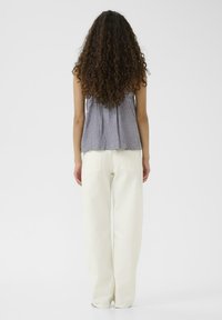 Szary bezrękawnik o subtelnym wzorze w połączeniu z kremowymi szerokimi spodniami. Stylizacja ma luźny krój i brak widocznych akcentów.