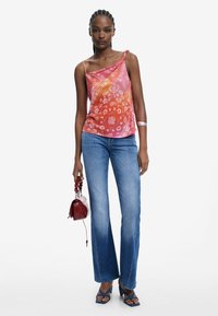 Flerfärgad silketopp med blommönster, asymmetrisk halsringning, ihopparad med ljusblå jeans och blå sandaler. Liten röd handväska som accessoar.