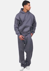 Grau Hoodie und passende Hose aus weichem Stoff, mit einer Front-Kängurutasche und dezentem Branding, kombiniert mit weißen Sneakers.