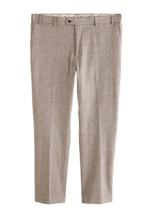 Junger Mann steht auf Steinstufen, trägt ein korallenfarbenes Langarmshirt, beige karierte Hose und schwarze Schuhe vor einem weißen Wandhintergrund.