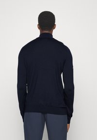 Navy blue knit sweater with a high collar, long sleeves, and a ribbed texture. Trim fit and minimalistic design, no visible logos or patterns.