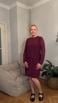 Burgunder rød kjole med lange, gjennomsiktige ermer og belte i midjen. Glatt stoff, knelang, kombinert med svarte flate sko med spenne-detaljer.