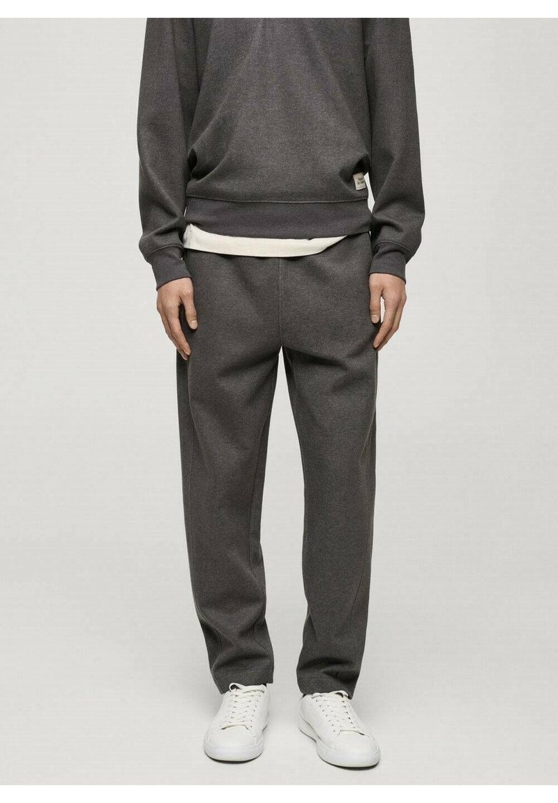 Sweat-shirt gris et pantalon assorti en tissu doux, avec une coupe décontractée et un t-shirt blanc en dessous. Porté avec des baskets blanches.