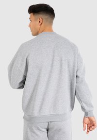Sweatshirt gris avec un col ras du cou, coupe décontractée et poignets et ourlet côtelés. Texture douce et design minimal, idéal pour une tenue décontractée.